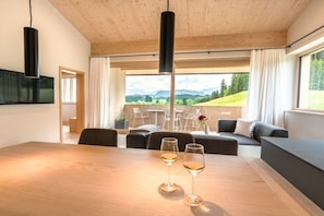Un espace repas moderne avec une table en bois, deux verres à vin et une vue sur l’extérieur.