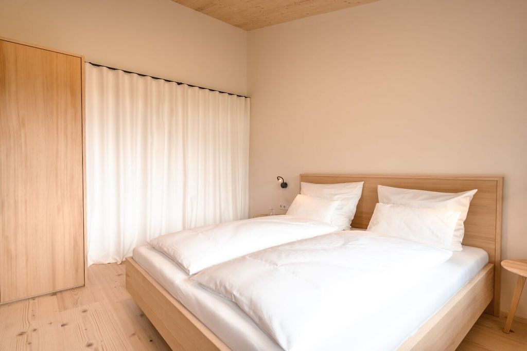Ein Schlafzimmer mit einem hölzernen Bett, weißer Bettwäsche, einem Holzschrank und einem Vorhang.