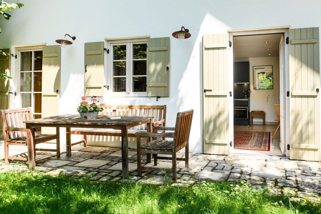 A patio with a wooden table and chairs, a potted plant, and a door leading to an interior space.