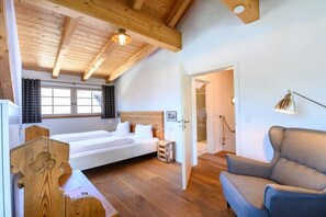 Ein Schlafzimmer mit Holzboden, einem Bett, einem Stuhl und einer Tür zu einem anderen Raum.