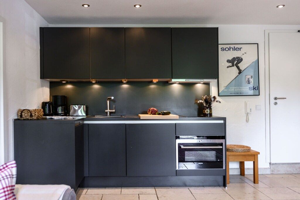 Une cuisine moderne avec des meubles de couleur sombre, un four encastré et un petit îlot central doté d’un évier.