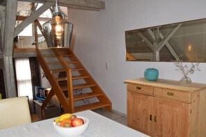 A room with a wooden staircase, a white table with a fruit bowl, a wooden cabinet, and a hanging light fixture. - at the Bornemann country house (Diemelsee-Adorf)