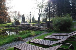 A tranquil outdoor area with a pond, wooden loungers, and a stone pathway. - at the Bornemann country house (Diemelsee-Adorf)