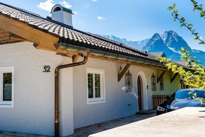 A building with a white facade, numbered 32, with a tiled roof and a view of mountains in the background. - Holiday apartment with 2 bedrooms (Garmisch-Partenkirchen)