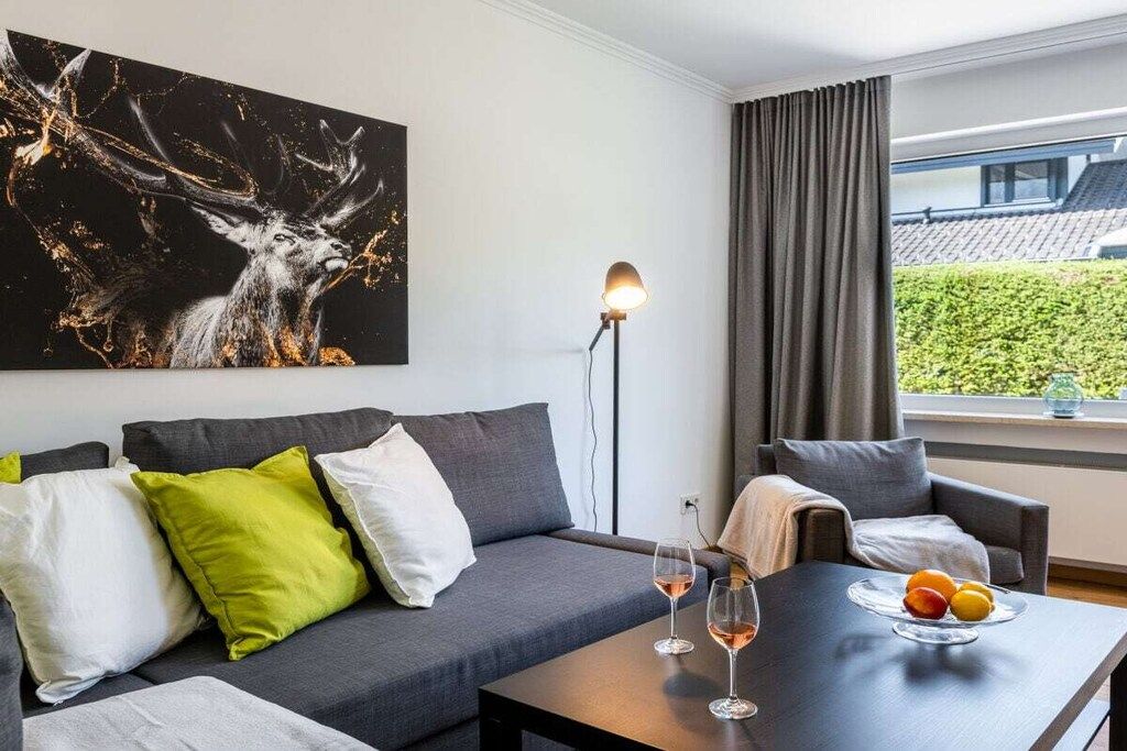 Uma sala de estar moderna com um sofá cinzento, uma mesa de centro com frutas, um abajur e um quadro grande de um veado.