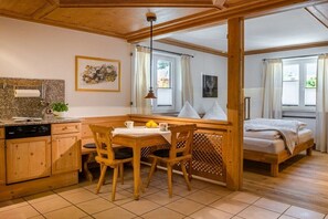 A cozy room with a wooden dining table, chairs, a bed, and a window with curtains. - Holiday apartment with 2 bedrooms (Garmisch-Partenkirchen)