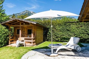 Eine Holzhütte mit einer Terrasse, einem Liegestuhl und einem großen Sonnenschirm.