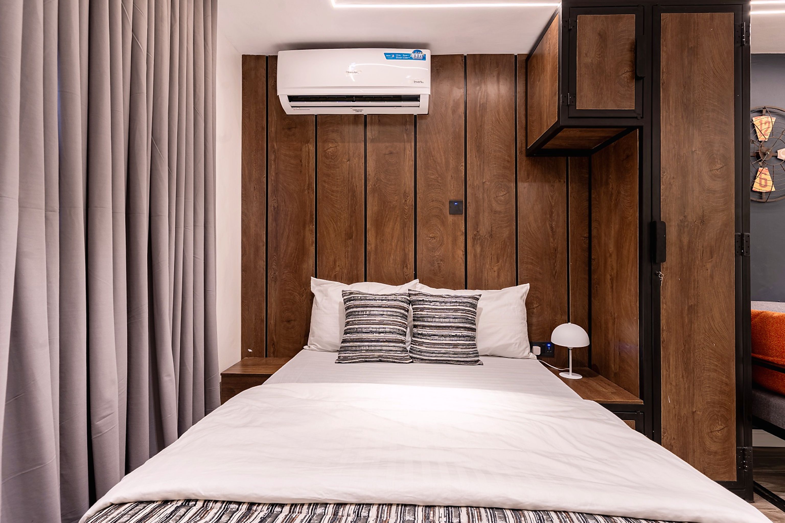 Ein Hotelzimmer mit Bett, Nachttisch, Klimaanlage und Holzschrank.