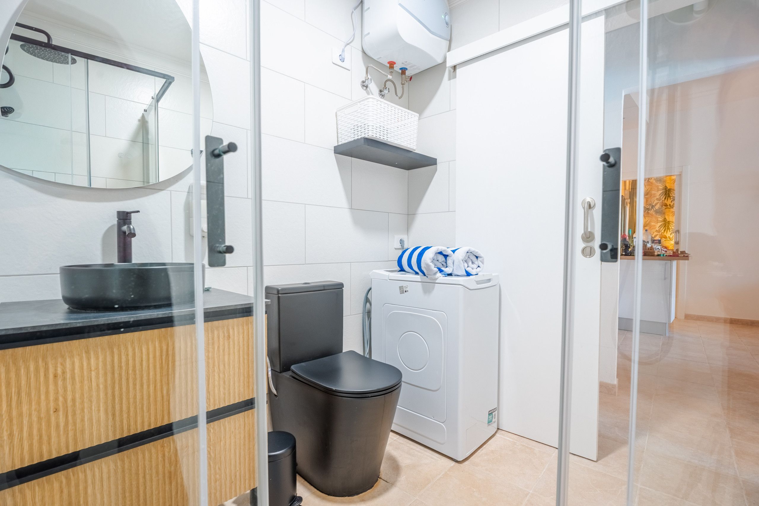 Une salle de bain moderne avec une paroi en verre, un lavabo, des toilettes, un lave-linge et un miroir.