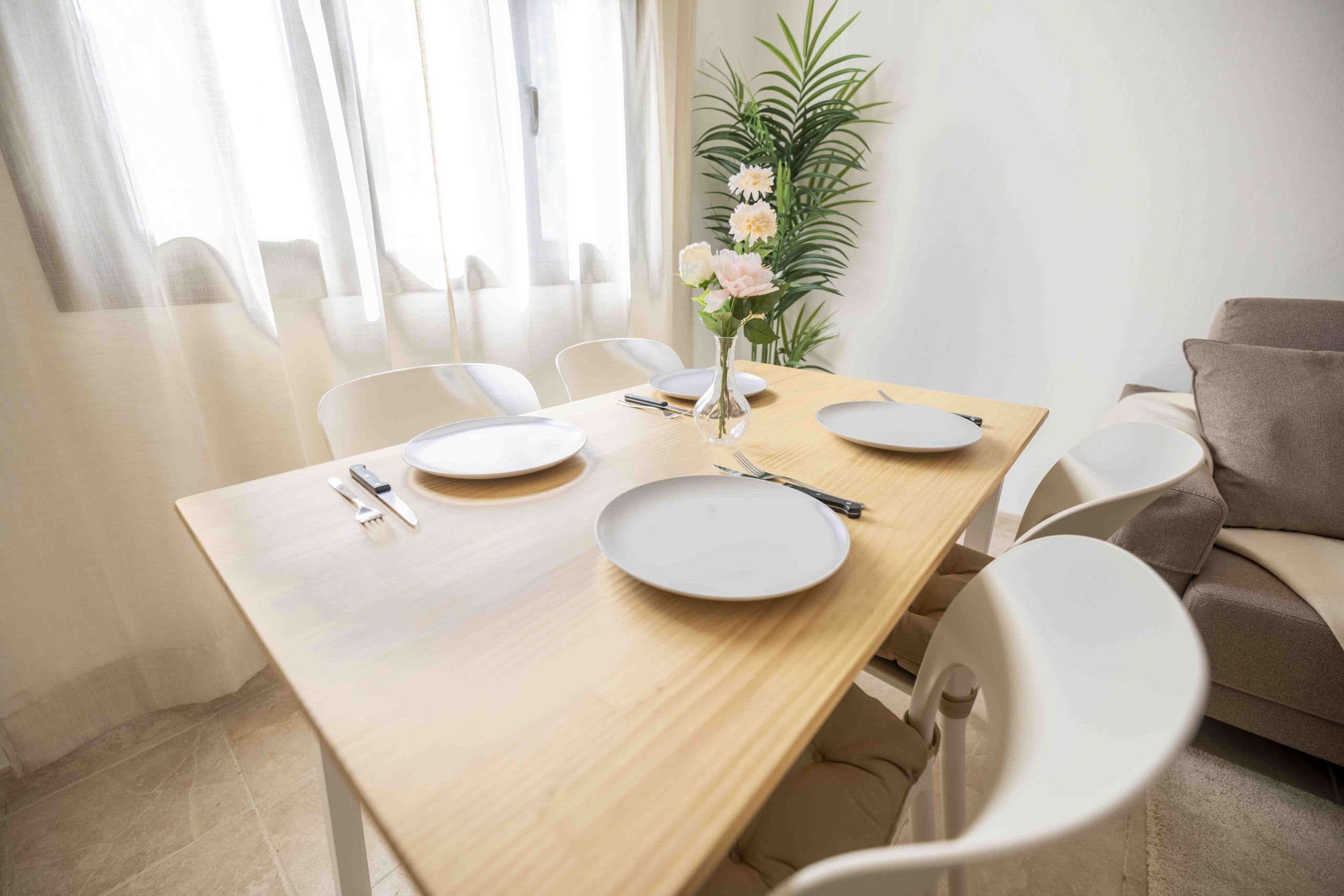 A dining area with a wooden table, white chairs, a vase with flowers, and a plant.
