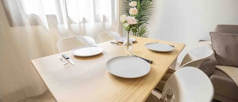A dining area with a wooden table, white chairs, a vase with flowers, and a plant.