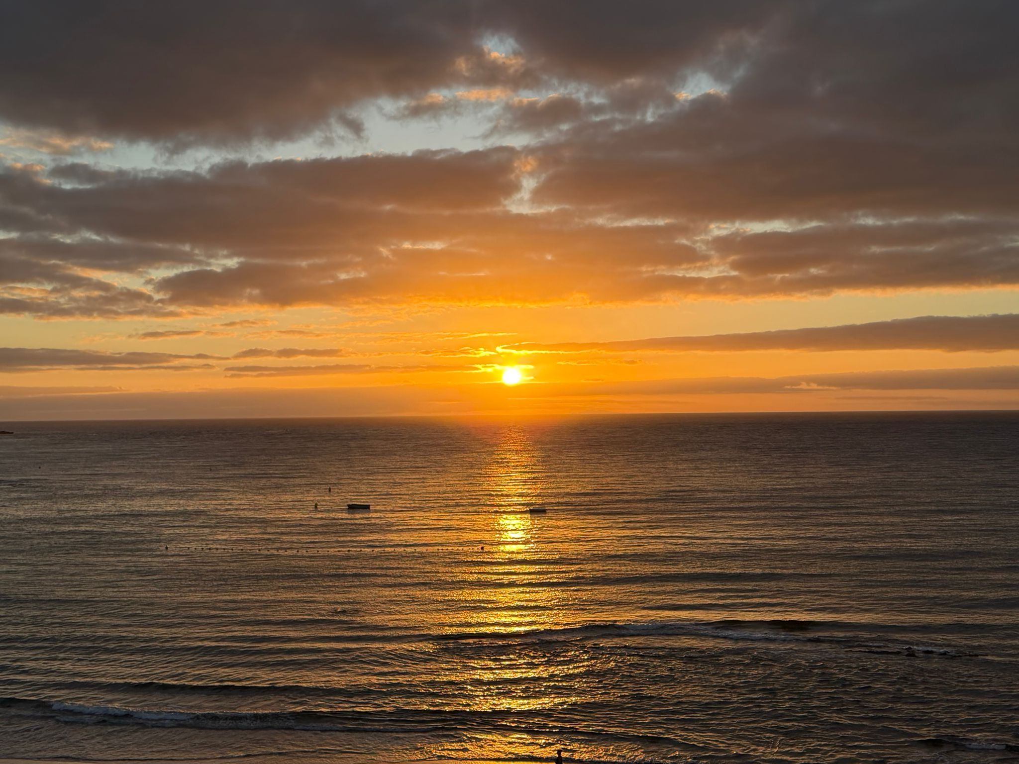 Un coucher de soleil sur l’océan, avec un bateau à l’horizon.