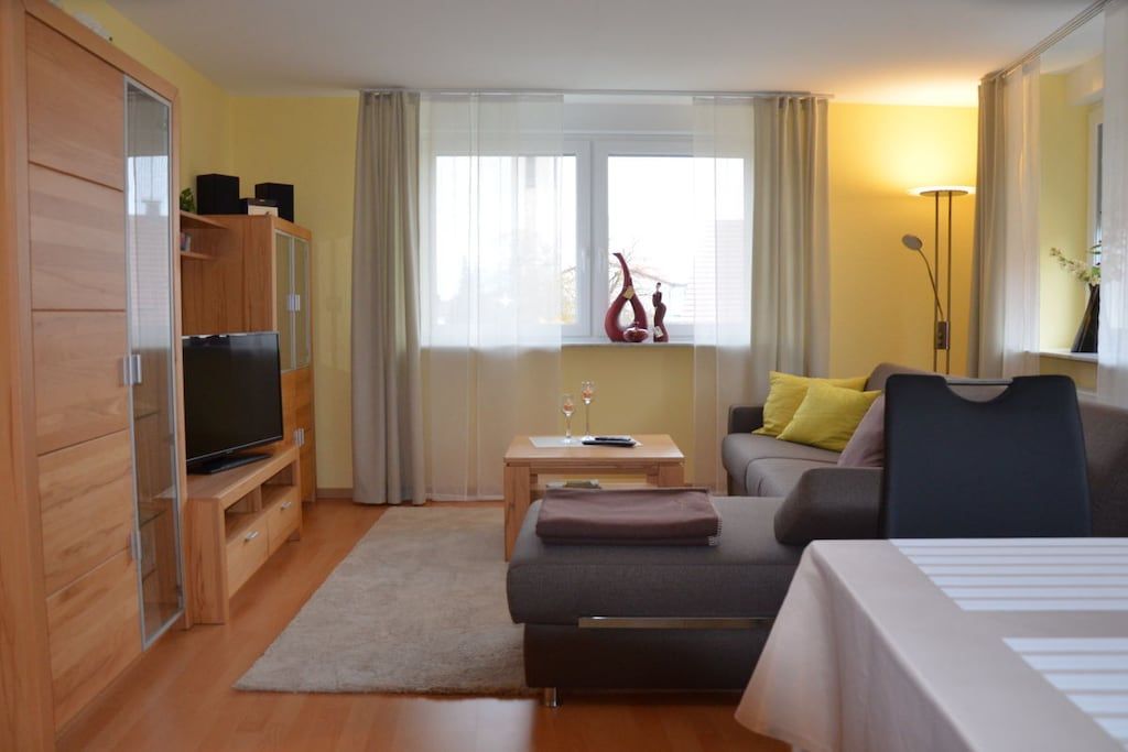 Een moderne hotelkamer met een bank, een bed, een televisie en een raam met gordijnen.
