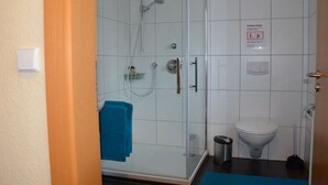 Ett badrum med en dusch som är avskärmad med glasväggar, en toalett och en papperskorg.