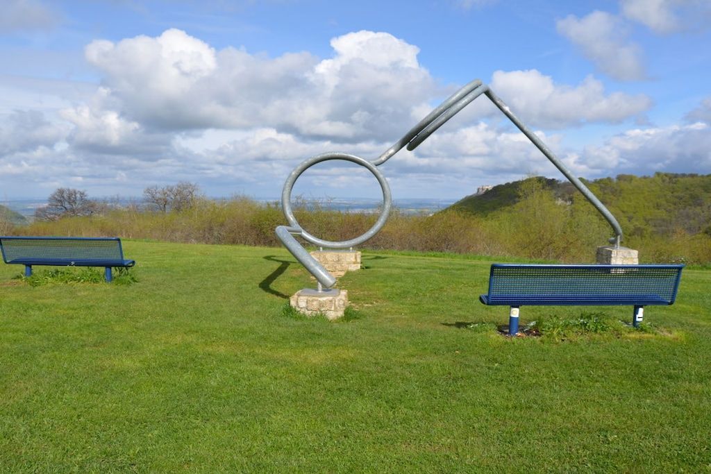 Een park met twee blauwe banken en een metalen sculptuur.