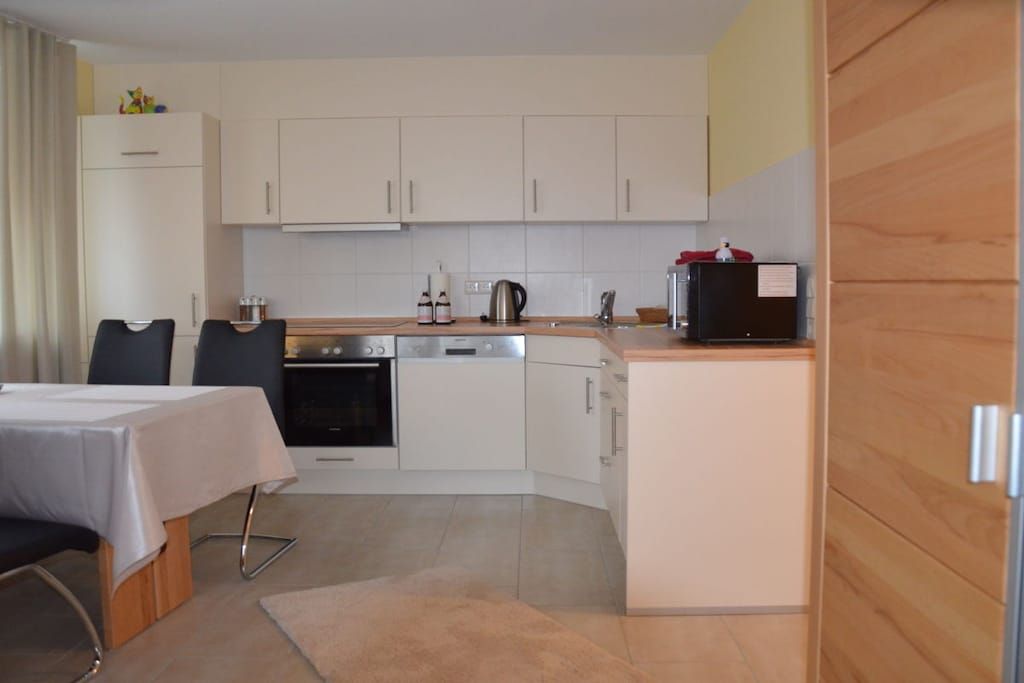A compact kitchen with white cabinets, a stove, a sink, and a small refrigerator.