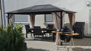 En uteplats med ett bord och stolar, en grill och en överbyggd sittplats.