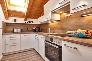 A modern kitchen with white cabinetry, a wooden countertop, and a built-in oven. - Alpklang Apartment #2 (Garmisch-Partenkirchen)