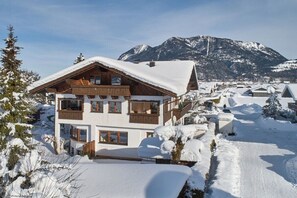 A multi-story chalet with a snow-covered roof, set against a mountainous backdrop. - Alpklang Apartment #2 (Garmisch-Partenkirchen)