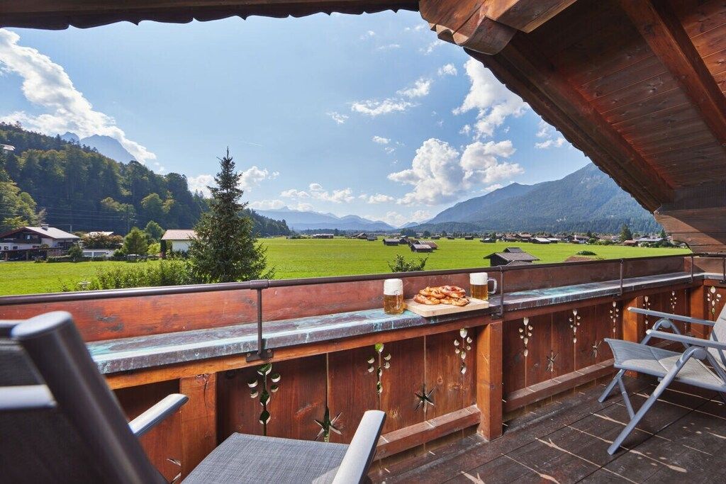 Ein Sitzbereich im Freien mit Blick auf ein grünes Feld und Berge.