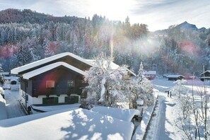 A snow-covered cabin with a sloped roof, surrounded by a forested area with snow-laden trees. - Alpklang Apartment #2 (Garmisch-Partenkirchen)