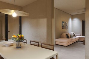 Un coin repas avec une table, des chaises et un panier de fruits. On y trouve également un canapé et un tableau accroché au mur.