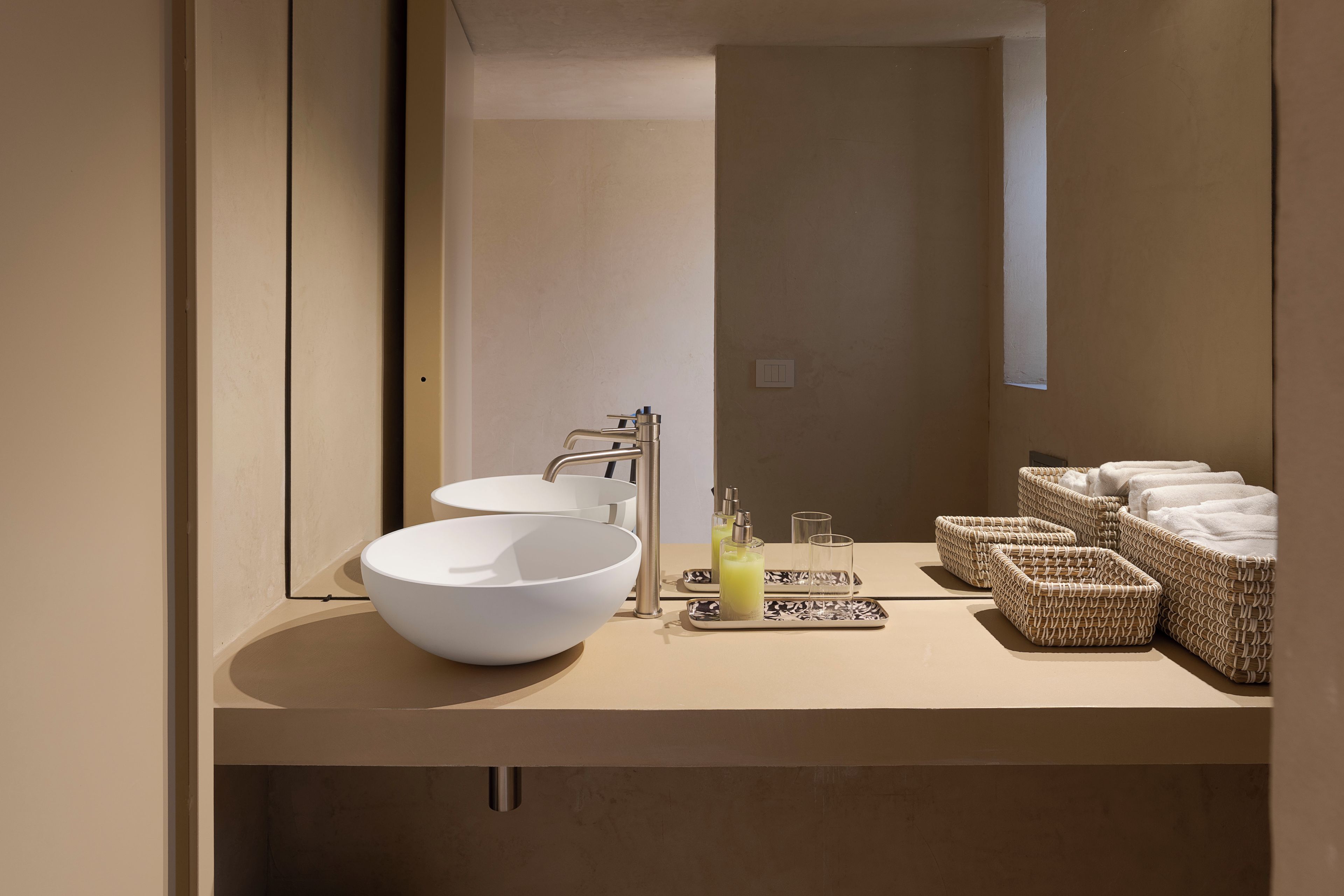 A modern bathroom with a large white sink, a mirror, and a tray with toiletries.