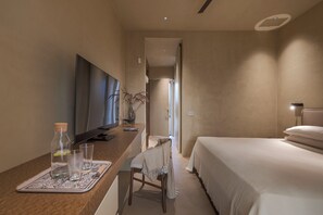 Une chambre d’hôtel avec un lit, un bureau avec une télévision, une chaise et une petite table avec des verres et une bouteille.