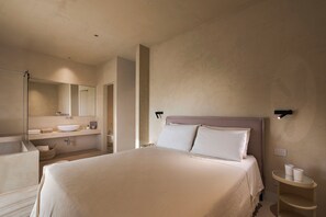 Ein modernes Hotelzimmer mit einem großen Bett, einem Badezimmer inklusive Waschbecken und Spiegel sowie einem kleinen Nachttisch mit Tassen.