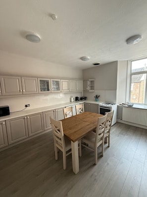 Une cuisine avec des meubles blancs, une table à manger en bois et une fenêtre.