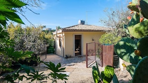 A house with a tiled roof, a gate, and surrounding vegetation. - Charming Villa with Lemon Garden Near Lido di Noto Beach (Noto)