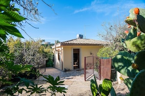 Uma casa com telhado de cerâmica, portão e vegetação ao redor.