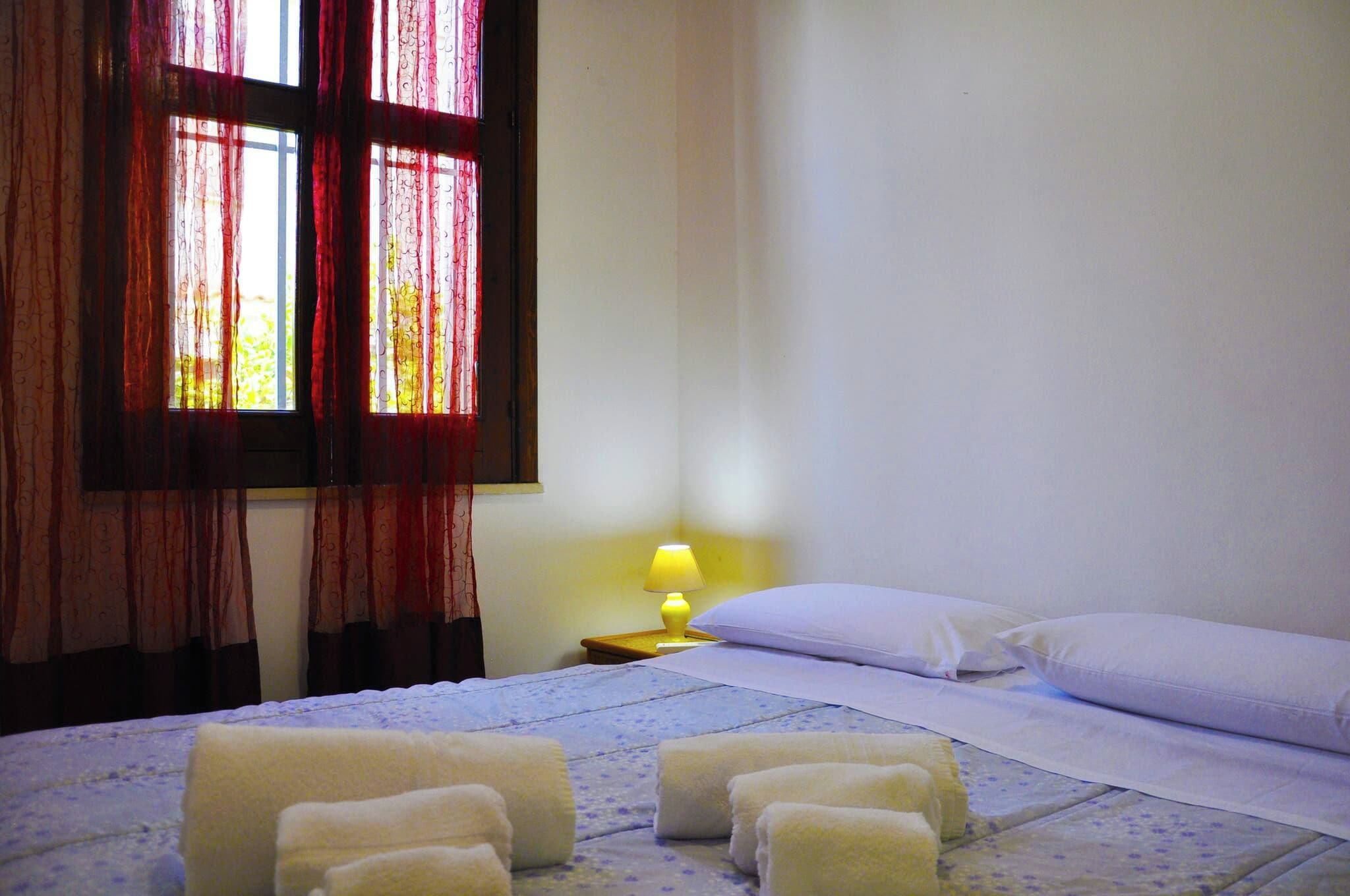 A hotel room with a bed, pillows, a nightstand with a lamp, and curtains.