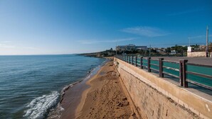 A coastal walkway with a concrete barrier and metal railing, leading to a sandy beach. - Charming Villa with Lemon Garden Near Lido di Noto Beach (Noto)