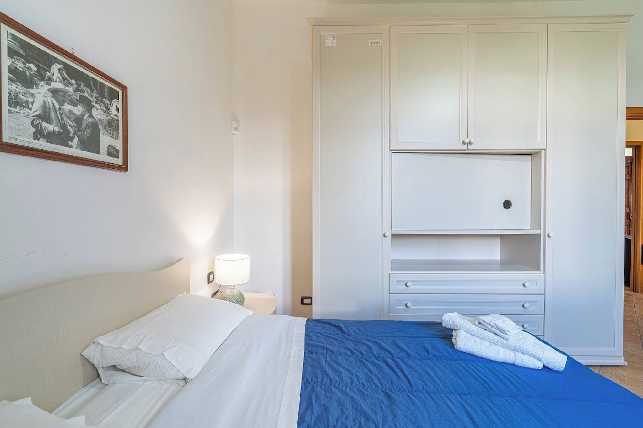 Un dormitorio con una cama, una mesita de noche, una lámpara, un armario y un cuadro en la pared.