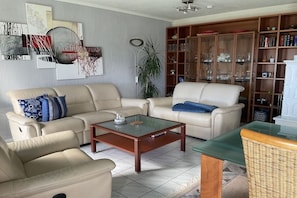 A living room with beige sofas, a glass coffee table, a bookshelf, and a floor lamp. - Dream view of the Rursee (Simmerath-Woffelsbach)