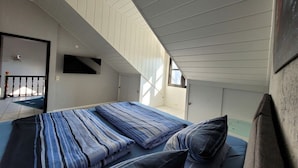 Quarto com cama, almofadas, televisão e janela.