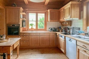 A wooden kitchen with a window, cabinets, a dishwasher, and a countertop. - Holiday home with 3 bedrooms (Weitnau-Hellengerst)
