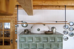 Une cuisine avec un poêle vert, des ustensiles de cuisine suspendus et un plafond en bois.