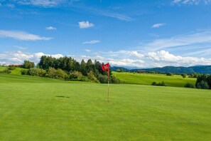 A golf course with a red flag on a flagstick, surrounded by green grass and trees under a clear sky. - Holiday home with 3 bedrooms (Weitnau-Hellengerst)