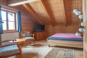 Quarto de cabana de madeira com cama, televisão, cadeira e mesa.
