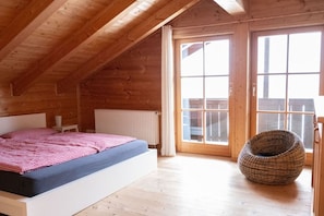 A wooden cabin bedroom with a bed, a radiator, and a large window. - Holiday home with 3 bedrooms (Weitnau-Hellengerst)