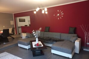 A modern living room with a red accent wall, a grey sofa, a coffee table with a vase, and a wall clock. - Holiday apartment with 3 bedrooms (Bacharach- Henschhausen)