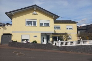 Een gebouw met twee verdiepingen, voorzien van een plat dak, een hoofdingang met deur en een klein portaal met een balustrade.