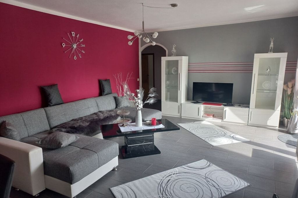 Una sala moderna con un sofá gris, una mesa de centro negra y una pared roja de acento.