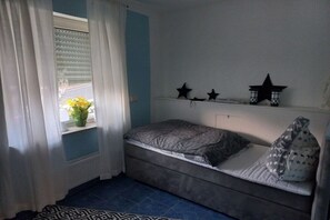 Een slaapkamer met een bed, een raam met gordijnen, een plankje met decoraties in de vorm van sterren en een potplant.
