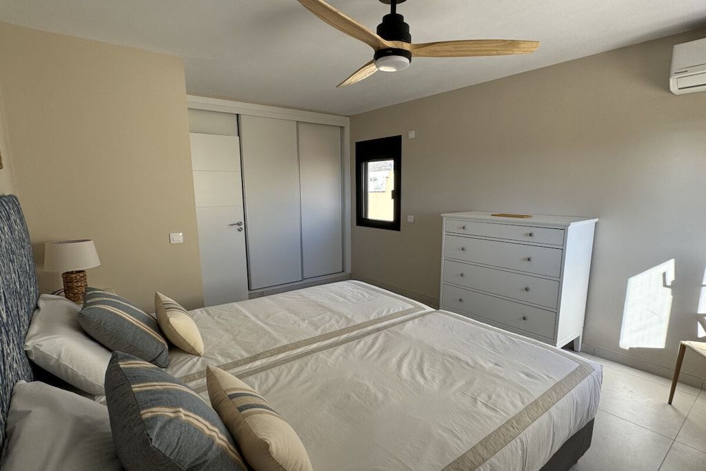 Ein Schlafzimmer mit Bett, Kommode, Deckenventilator und Fenster.