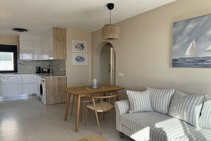 A modern kitchen with a dining area, a sofa, and artwork on the walls. - Apartment Tortuguero (Morro Jable, Jandia, Fuerteventura)