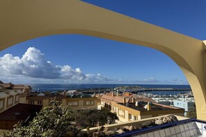 A coastal view through a yellow archway overlooking a marina with boats and buildings. - Apartment Tortuguero (Morro Jable, Jandia, Fuerteventura)