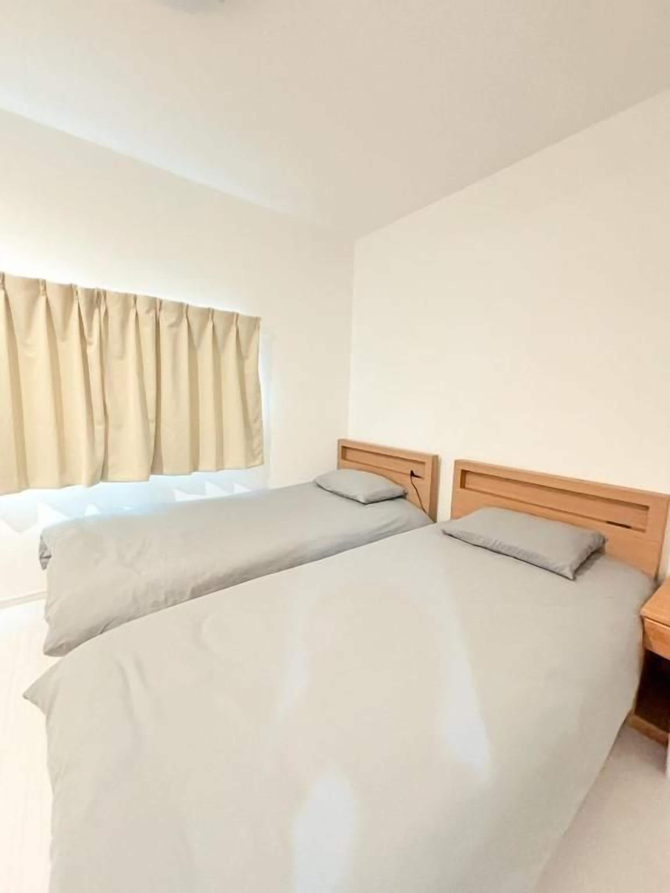 A room with two beds, a window with curtains, and a wooden headboard.